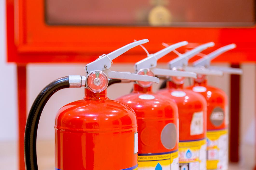 Close-up of a row of red fire extinguishers with silver handles and black hoses mounted against a bright red wall.