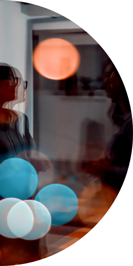 Blurred image of two people conversing indoors with colorful spherical lights in the foreground.