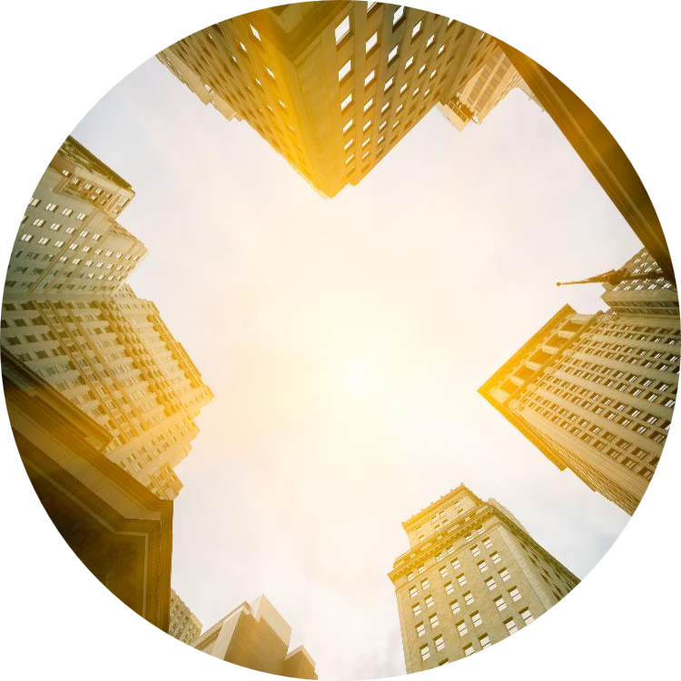 Upward view of tall city skyscrapers surrounding a bright sky, illuminated by warm sunlight.