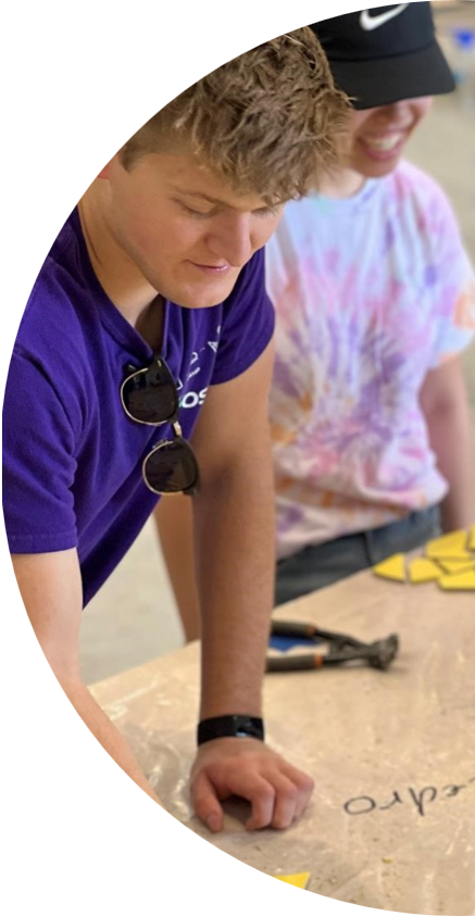 Two people working together at a table on a hands-on project, with tools and materials spread out.