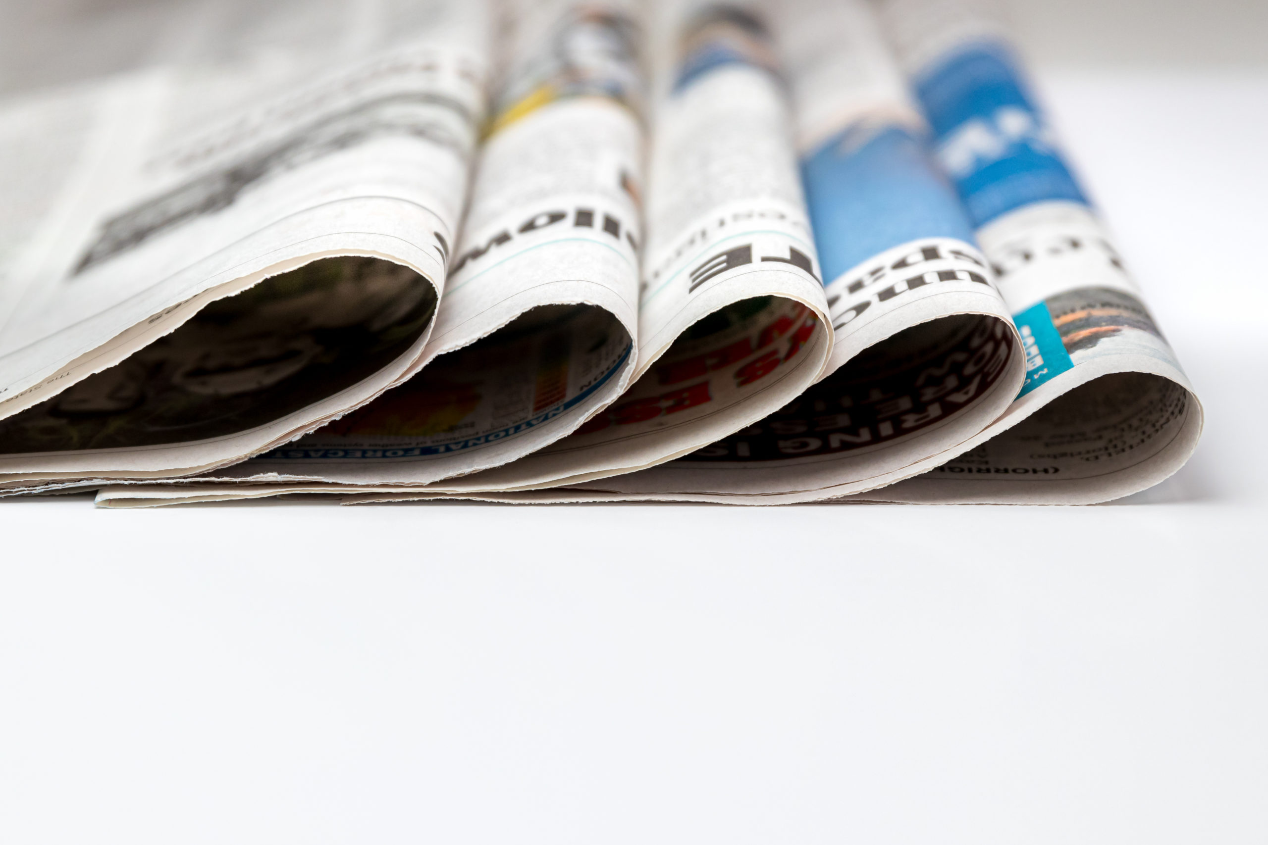 Close-up of several rolled newspapers stacked side by side on a white surface.
