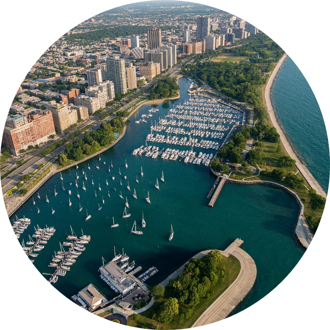 Oval-cropped aerial view of Belmont Harbor with a large marina filled with sailboats, high-rise buildings, and a long shoreline along a blue lake.
